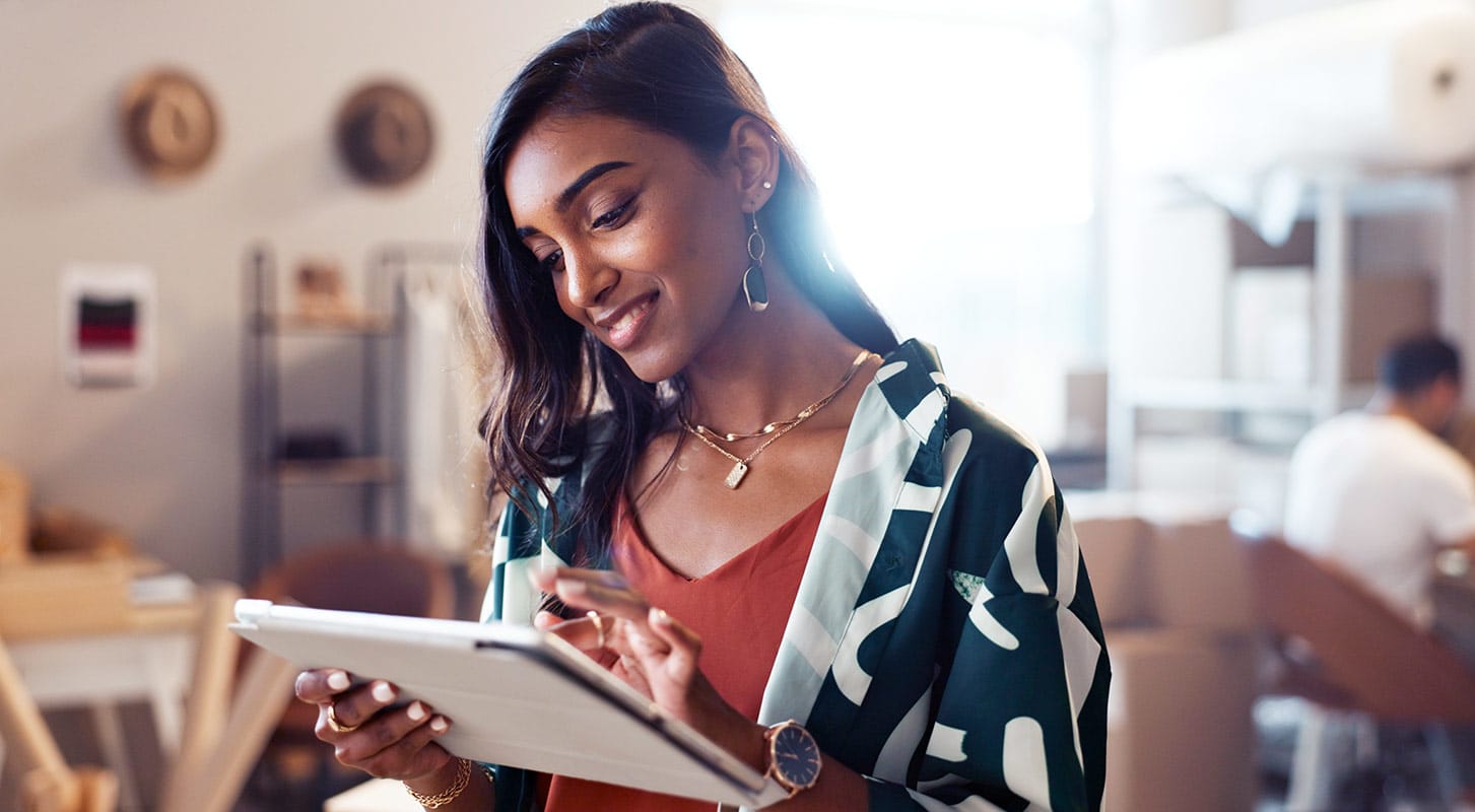 A woman uses a tablet in a coffee shop, surrounded by a cozy atmosphere.